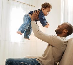 Time together. Good-looking loving caring father smiling and amusing his son while sitting on the couch